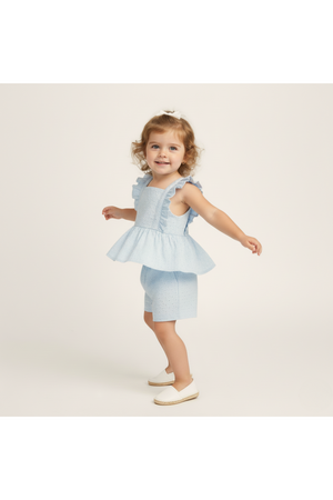 A young girl is wearing a light blue organic cotton eyelet flutter top and matching shorts set.