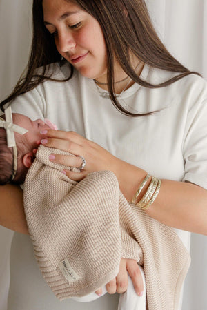 A woman gently cradles a baby wrapped in a beige knit blanket, showcasing a serene and nurturing moment.