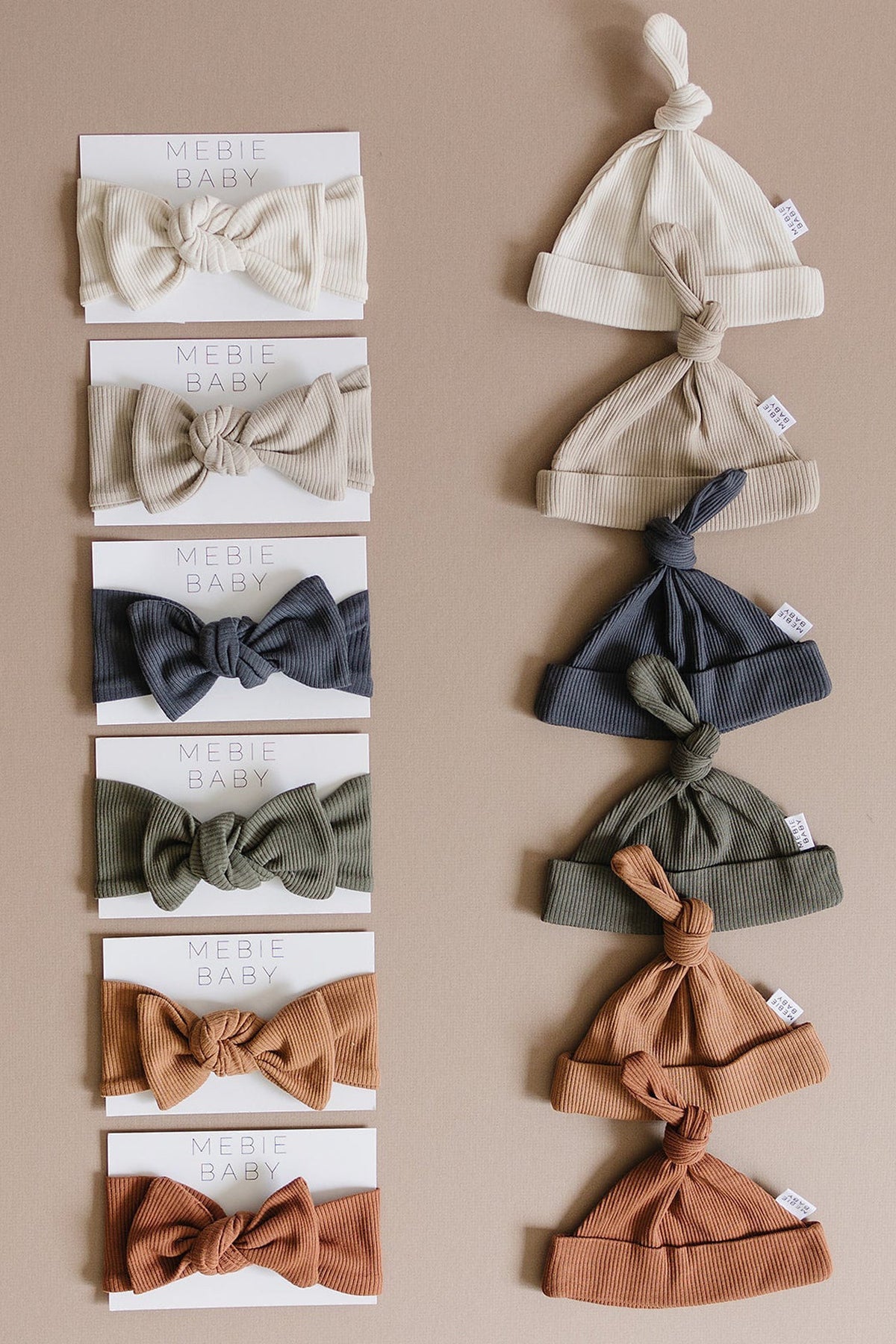 A collection of Mebie Baby ribbed knot hats and headbands in various earthy tones on a neutral background.