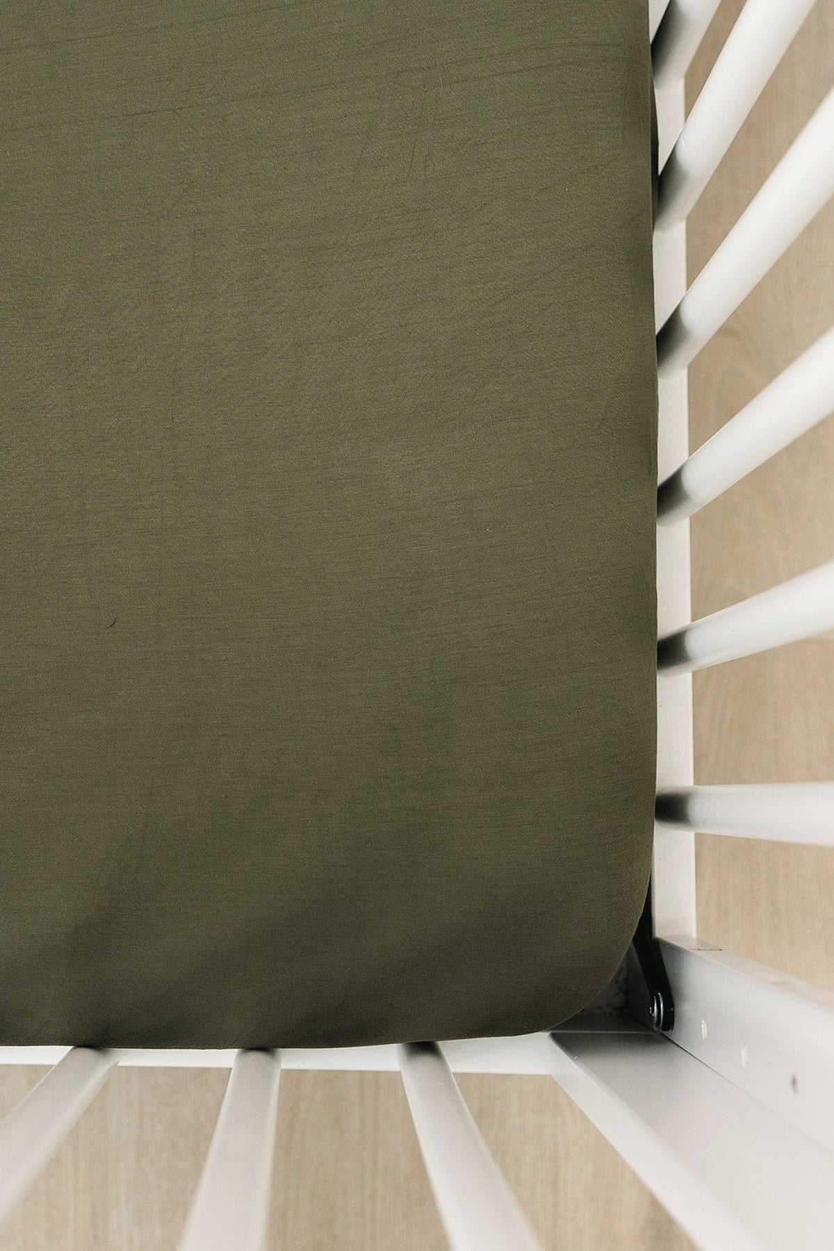 Olive green crib sheet on a white crib, showcasing smooth texture and snug fit.