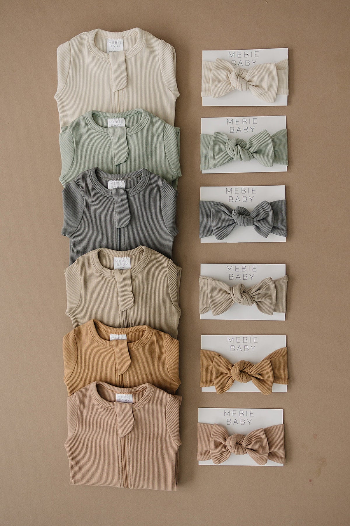 Ribbed baby pajamas in various earth tones, paired with matching knotted headbands, displayed on a brown background.