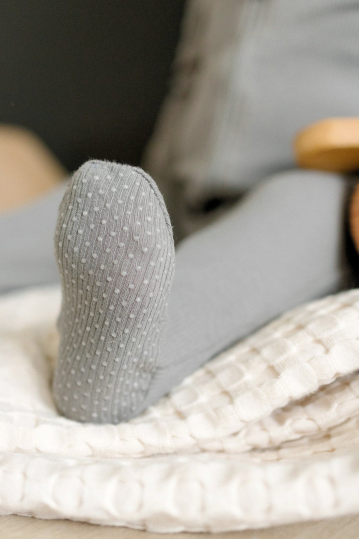 Close-up of a grey ribbed baby pajama foot on a textured white blanket, showcasing knit detail.