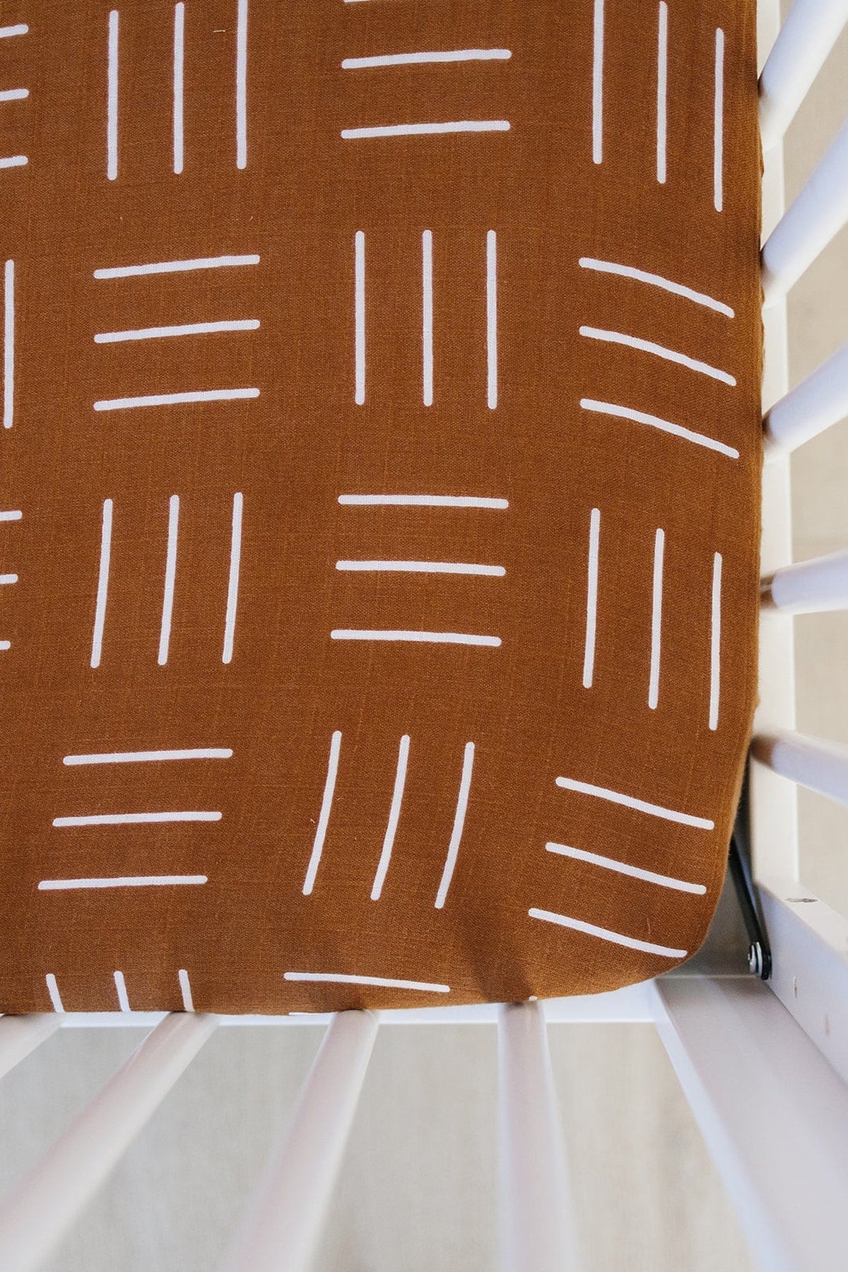 Mustard crib sheet with white mudcloth pattern on a white crib, showcasing simple design and soft fabric.