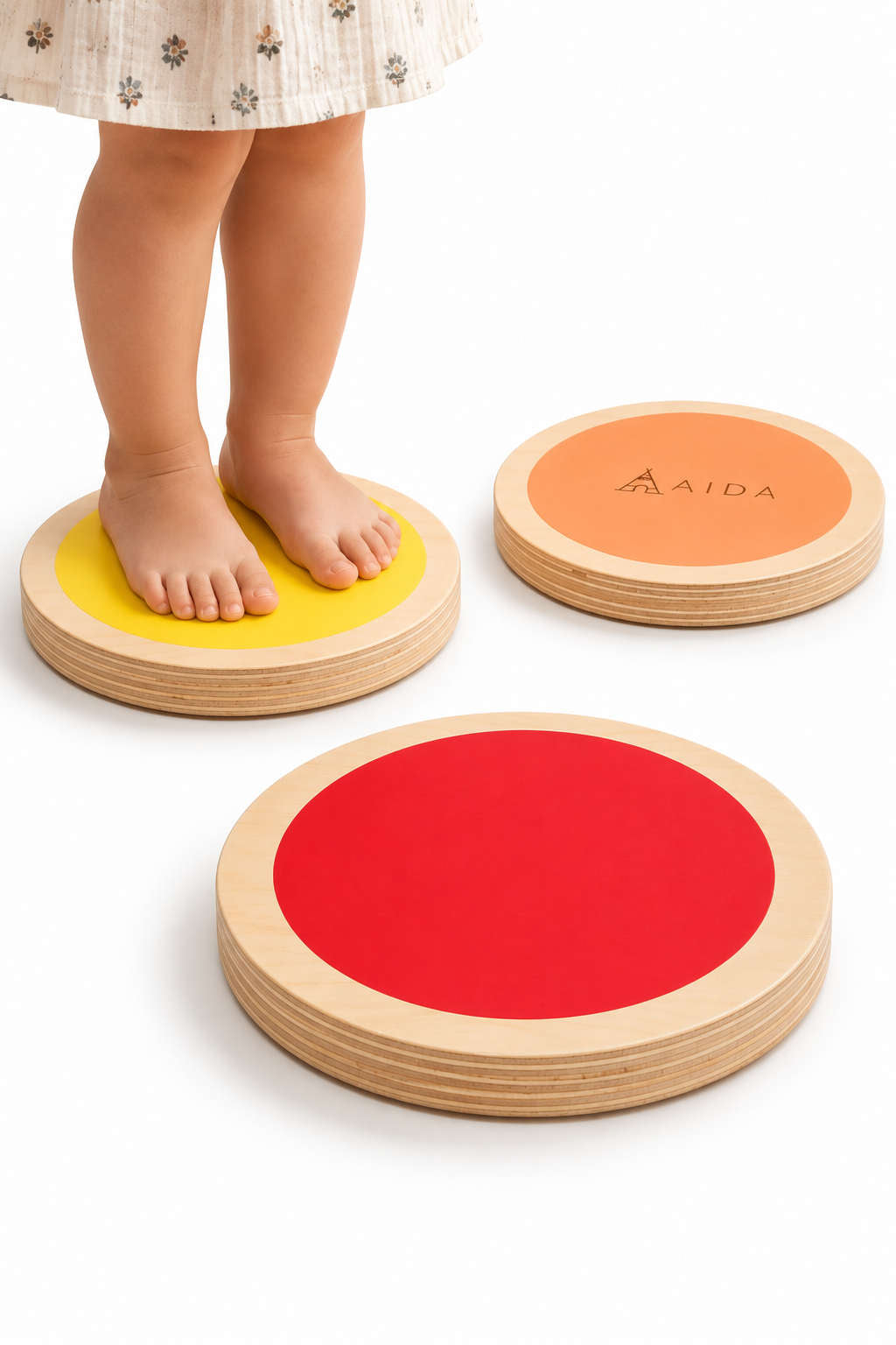 A child stands barefoot on colorful wooden stepping stones in yellow, orange, and red. The stones are made of sustainable materials, promoting playful movement and balance for young adventurers.