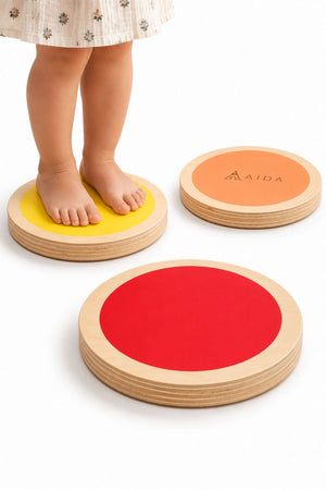 A child stands barefoot on colorful wooden stepping stones in yellow, orange, and red. The stones are made of sustainable materials, promoting playful movement and balance for young adventurers.