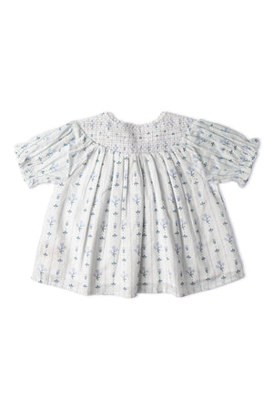 A light blue organic cotton smocked top features delicate floral embroidery and short puff sleeves. The airy design is suitable for sunny day outings, offering both comfort and style.