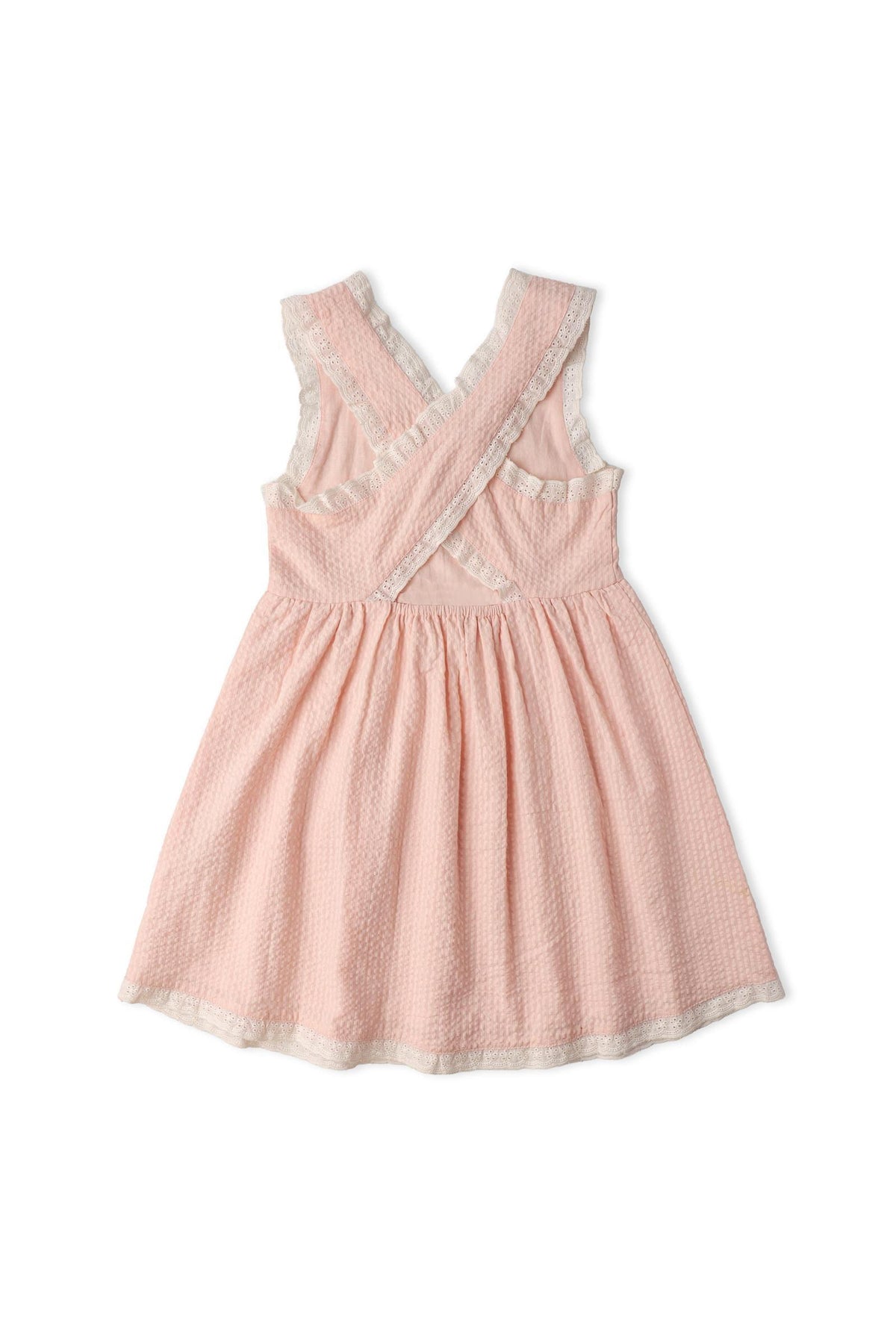 Back view of a blush pink organic cotton dress featuring criss-cross straps and a gently gathered skirt. The lightweight seersucker fabric adds a charming touch, perfect for warm weather.