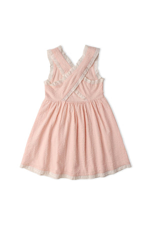 Back view of a blush pink organic cotton dress featuring criss-cross straps and a gently gathered skirt. The lightweight seersucker fabric adds a charming touch, perfect for warm weather.