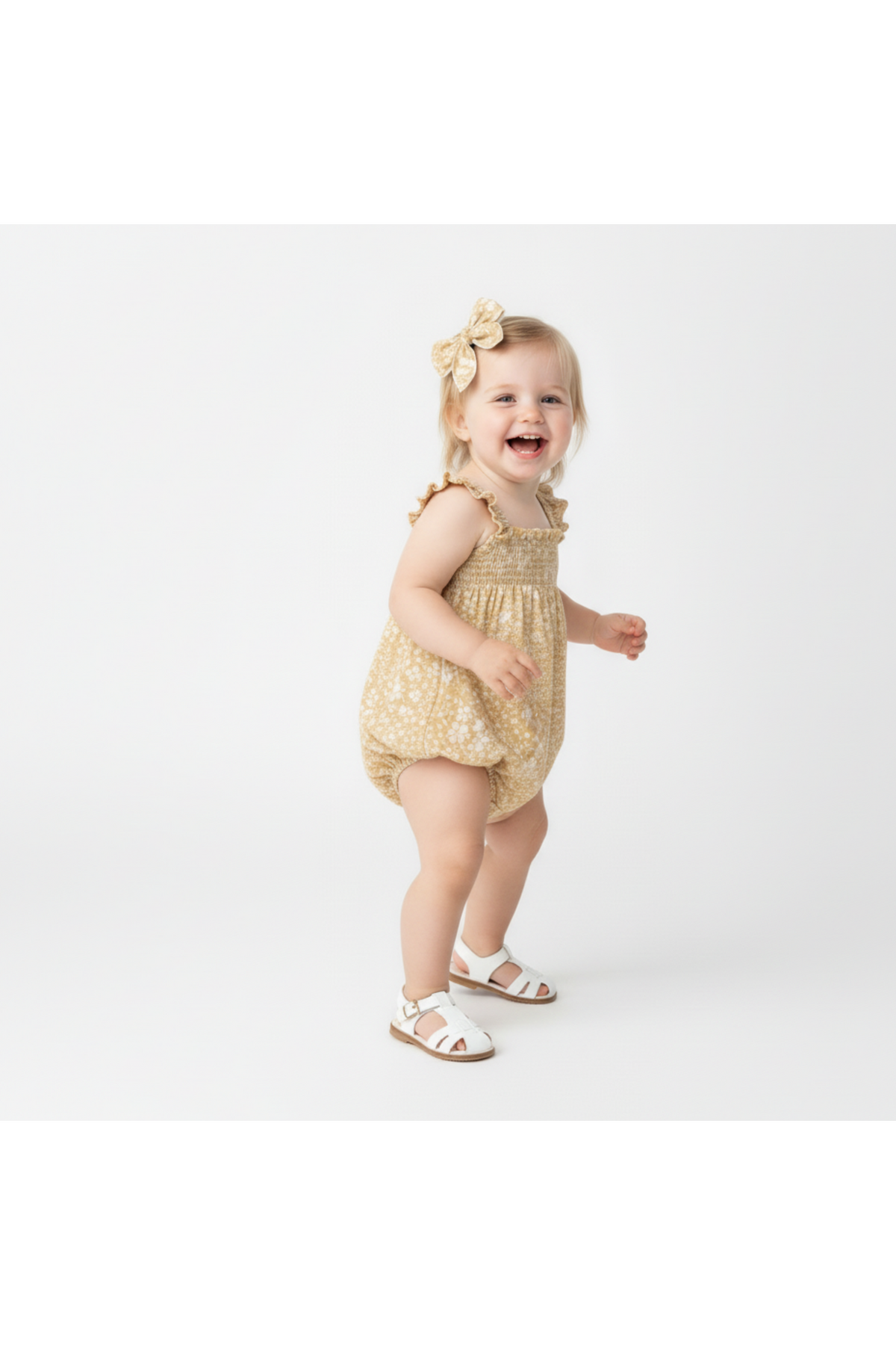 A joyful toddler wears a yellow floral ruffle sleeve bubble romper, paired with white sandals. The organic cotton fabric ensures comfort and breathability for active play.