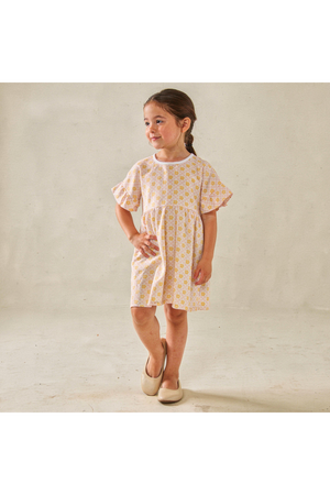 A young girl stands in a light yellow organic cotton dress featuring a playful floral print and dolman sleeves. The dress is designed for comfort and everyday wear.