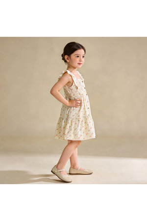 A young girl poses in a light floral dress featuring flutter sleeves and a tiered silhouette. The dress is made from organic materials, highlighting its sustainable and comfortable design.