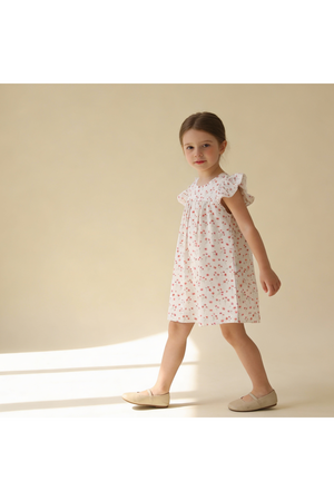 A young girl models a short sleeve dress with a floral pattern in soft pink and white. The flutter sleeves add a playful touch, perfect for warm, sunny days.