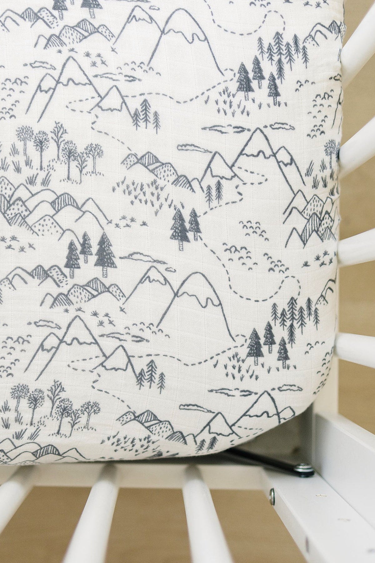 A muslin crib sheet featuring a monochrome mountain and tree design, neatly fitted on a white crib.