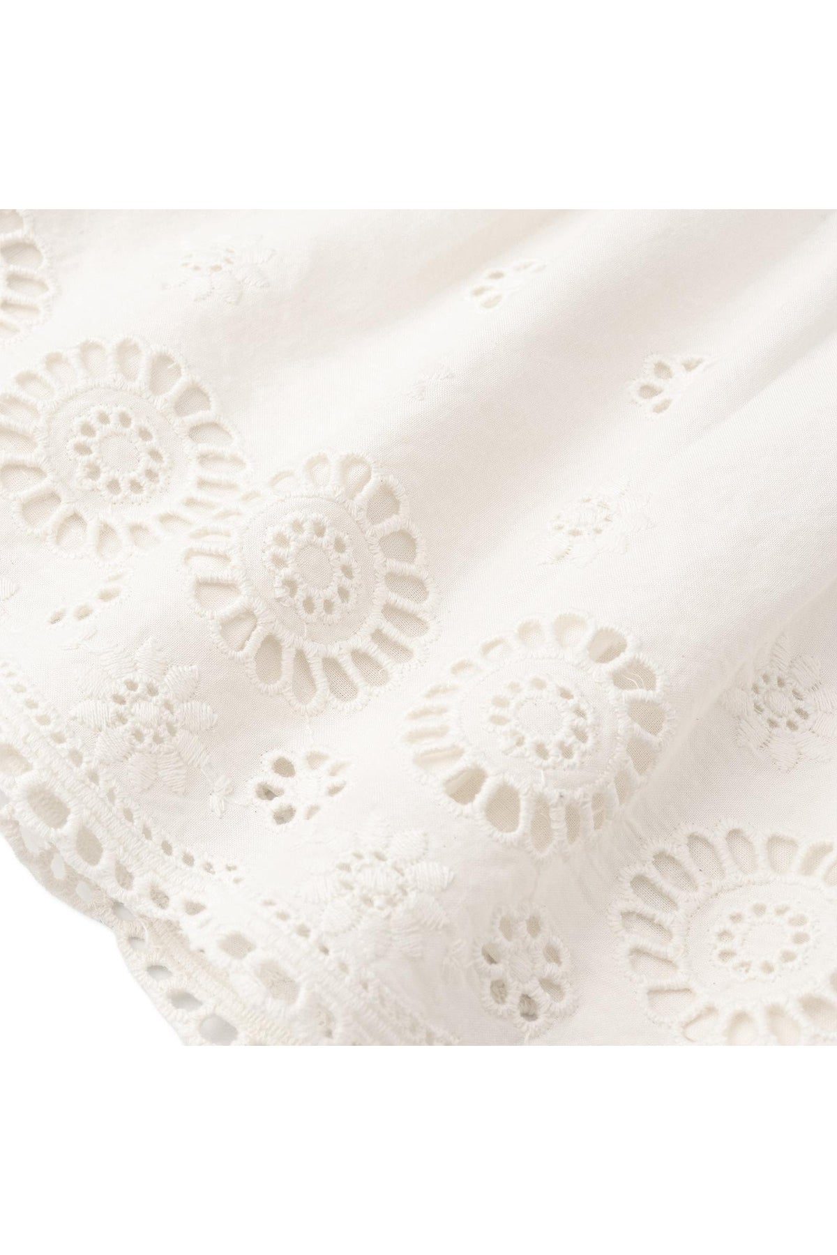 Close-up of delicate ivory organic cotton fabric featuring intricate eyelet embroidery and cutwork details. This sustainable material is perfect for creating lightweight, breathable clothing for warm-weather occasions.