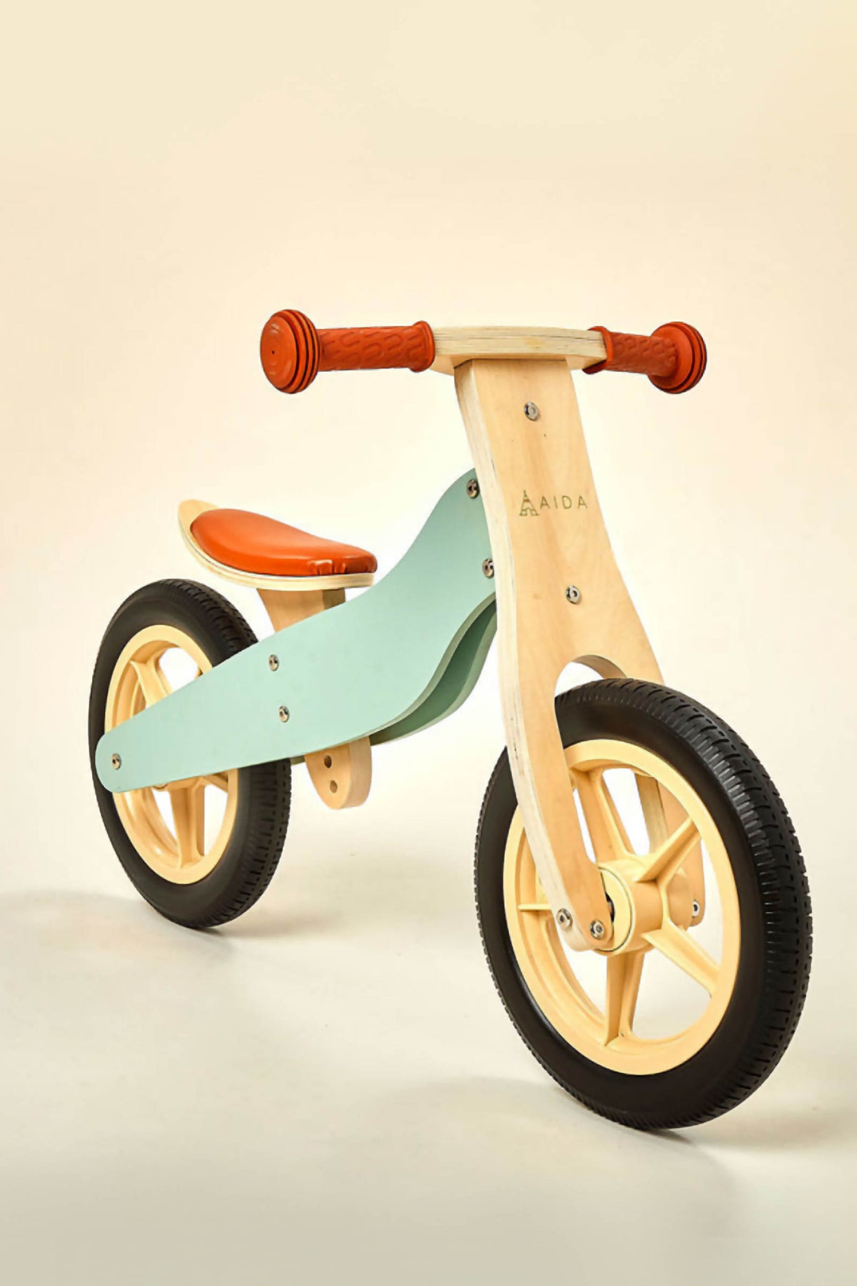 A wooden balance bike featuring a mint green frame, orange seat, and rubber tires. Designed for toddlers aged 2 to 4, it promotes coordination and confidence in young riders.