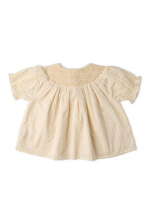 A soft, butter yellow organic cotton smocked top features a textured weave and puffed sleeves. The back showcases delicate smocking, perfect for sunny day outings.