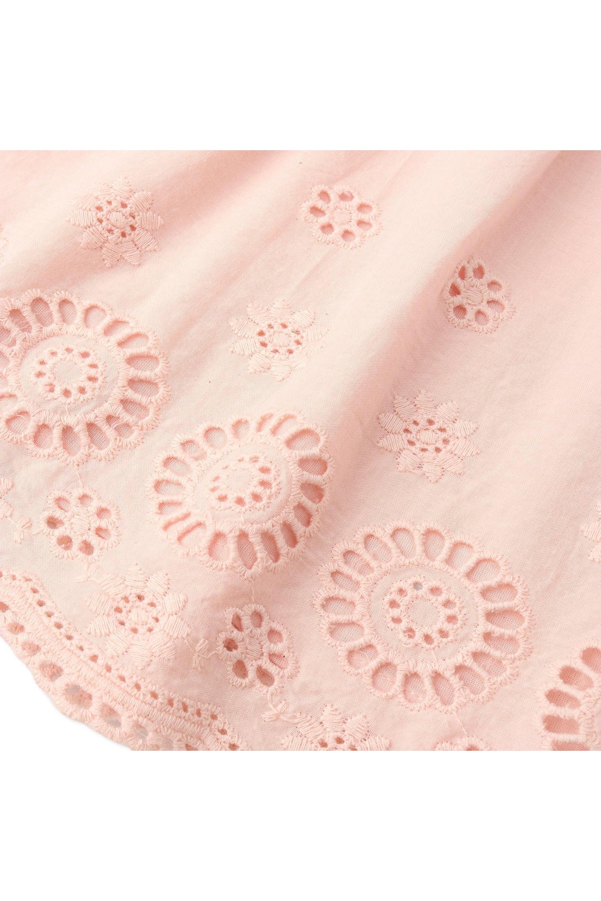 Close-up of delicate blush organic cotton fabric featuring intricate eyelet embroidery with floral designs, perfect for a light and airy top or pant set. Ideal for warm-weather outfits.