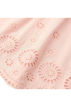 Close-up of delicate blush organic cotton fabric featuring intricate eyelet embroidery with floral designs, perfect for a light and airy top or pant set. Ideal for warm-weather outfits.