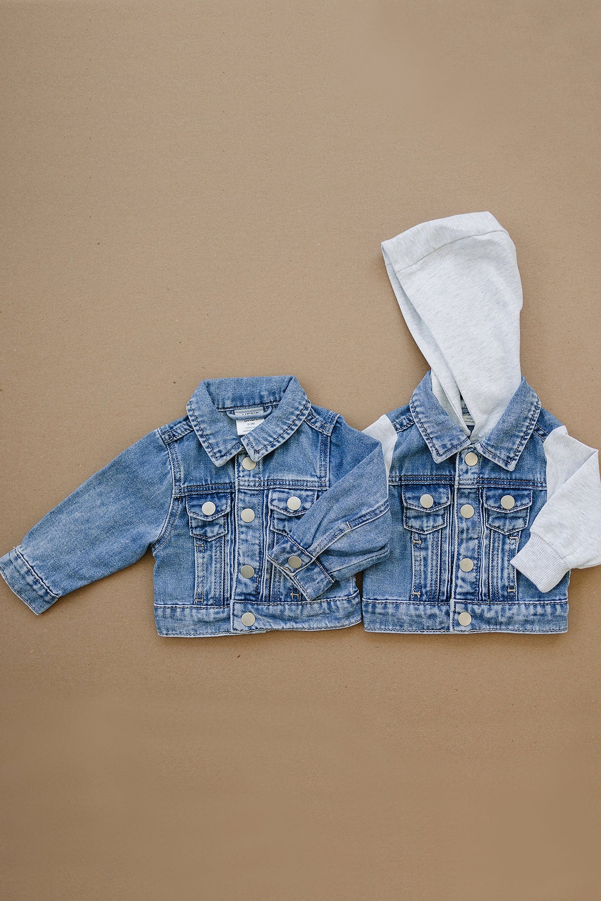 Two denim jackets for toddlers, one with grey hood and sleeves, displayed on a neutral background.