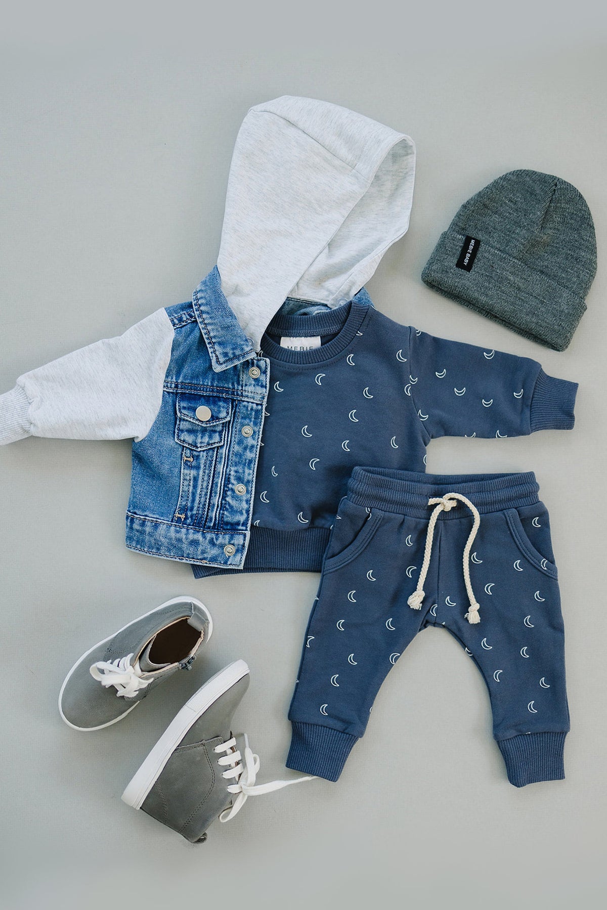 Baby outfit featuring a hooded jean jacket with grey sleeves, moon-patterned sweatshirt and pants, grey beanie, and sneakers.