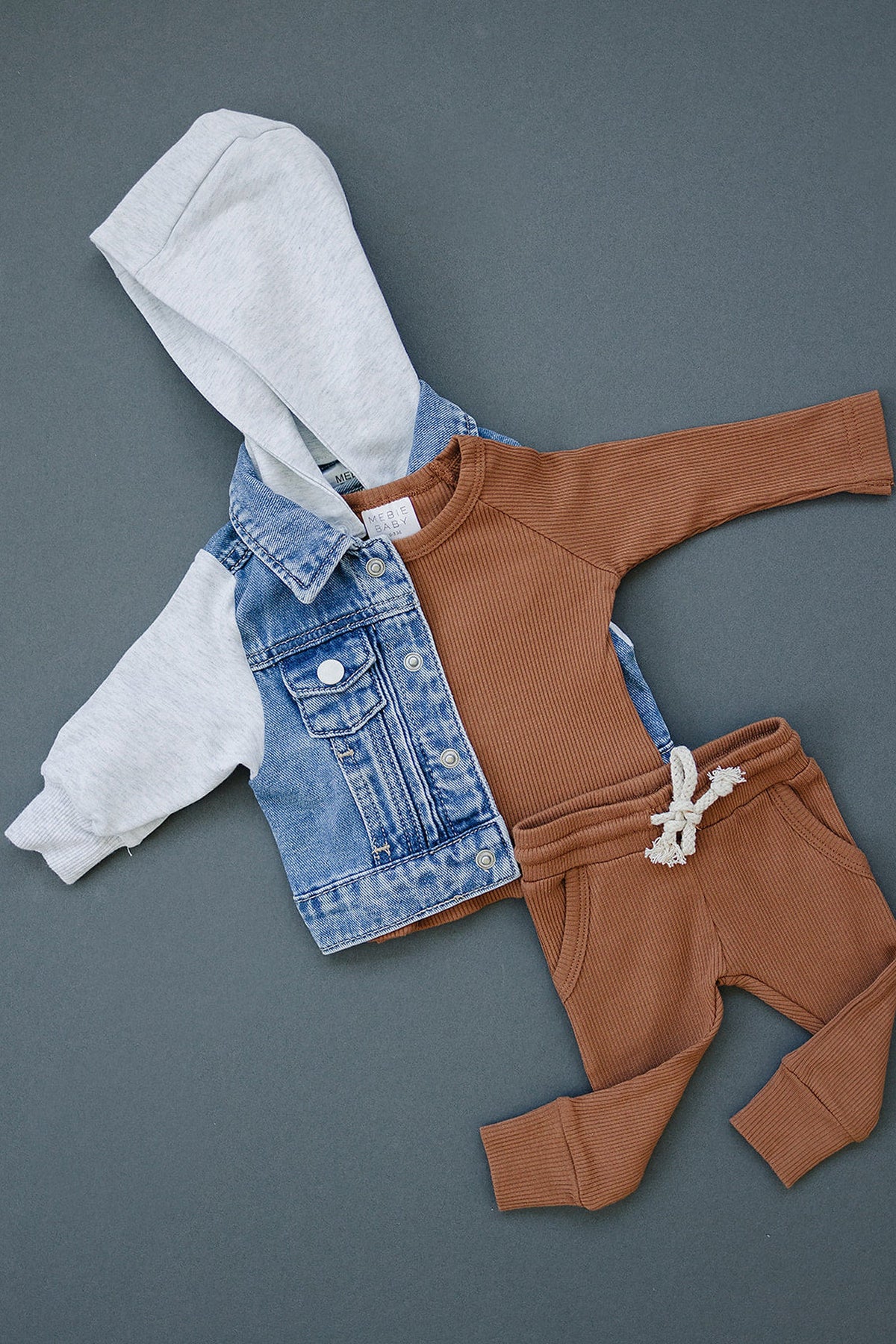 A baby outfit with a denim jacket featuring a gray hood and brown ribbed top and pants.