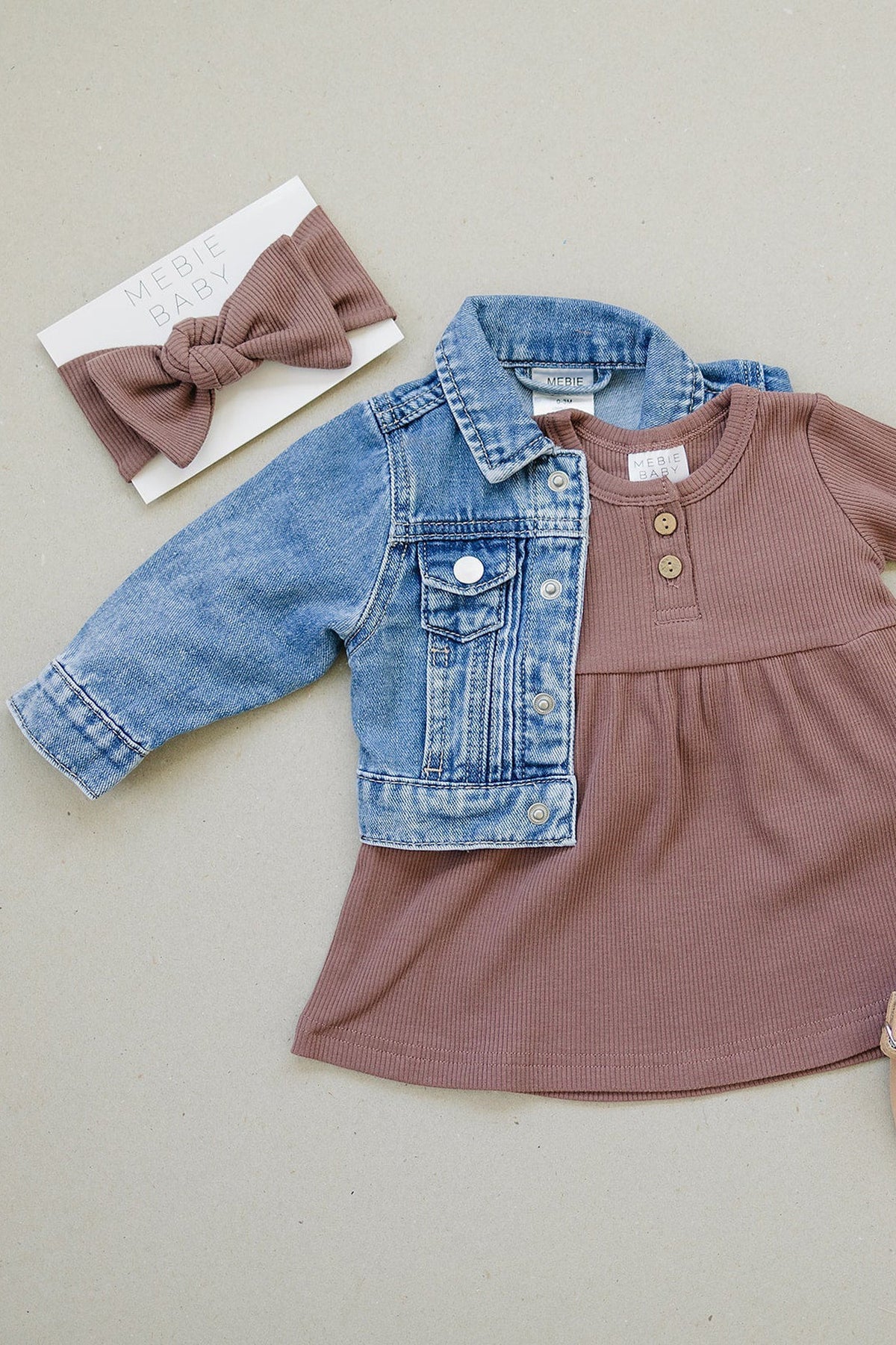 Blue denim jacket and brown dress with button details, accompanied by a matching brown headband on a beige background.