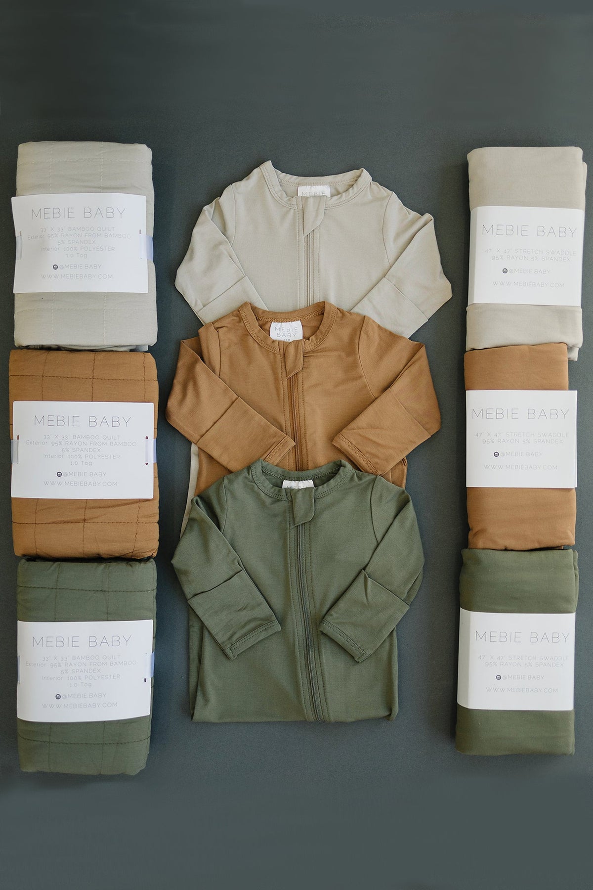Mebie Baby pajamas in beige, brown, and olive, surrounded by matching bamboo quilts and swaddles on a dark background.
