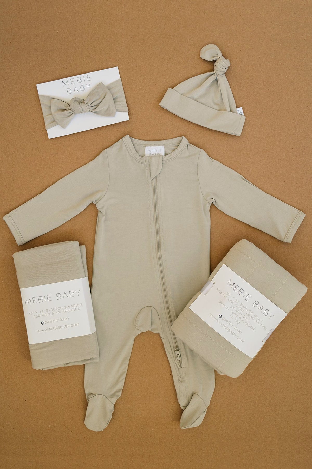 Mebie Baby oatmeal footed zipper pajama with matching hat and bow, displayed on a brown surface.