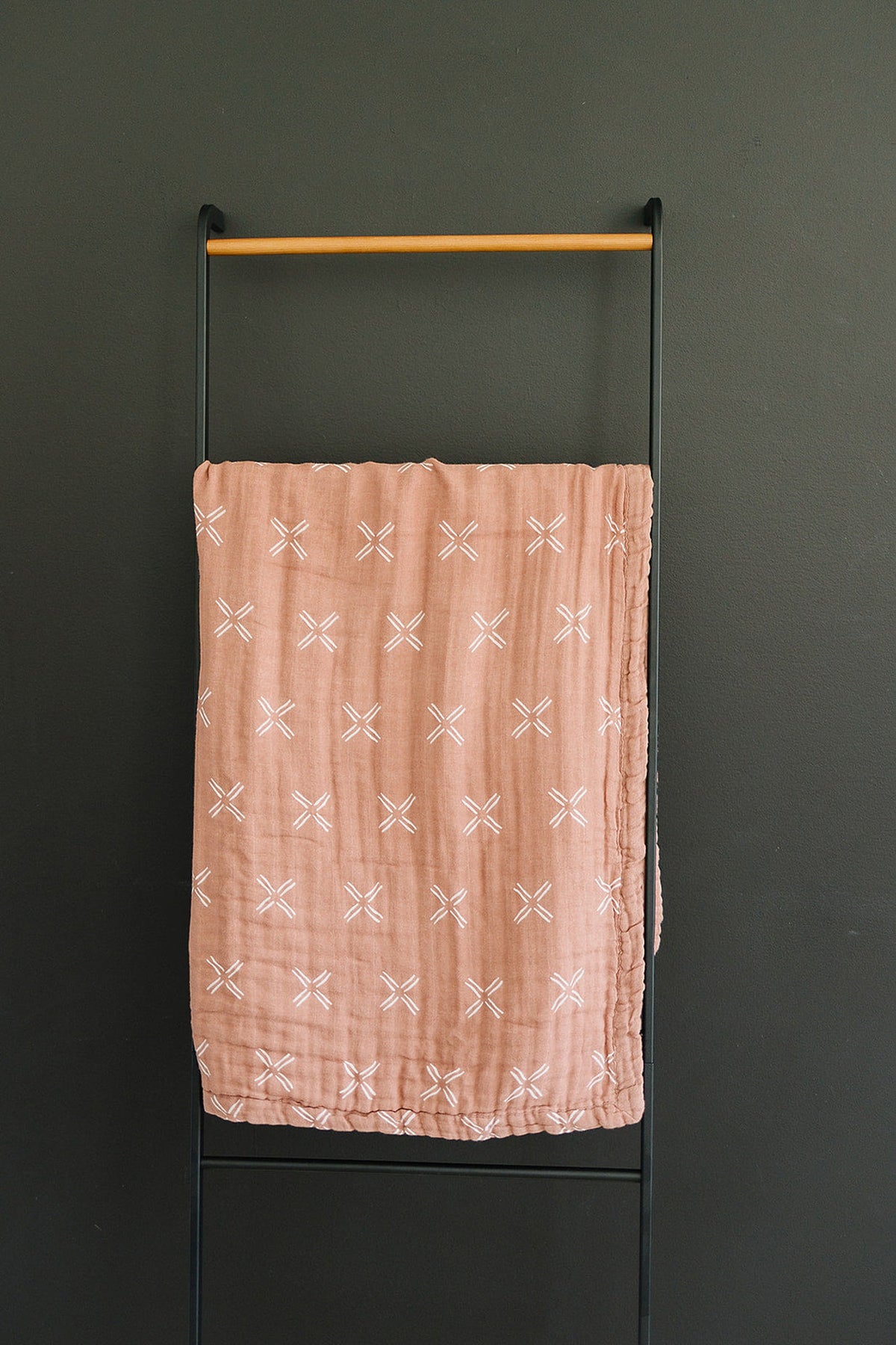 A peach-colored muslin quilt with white cross patterns hangs on a black metal rack.