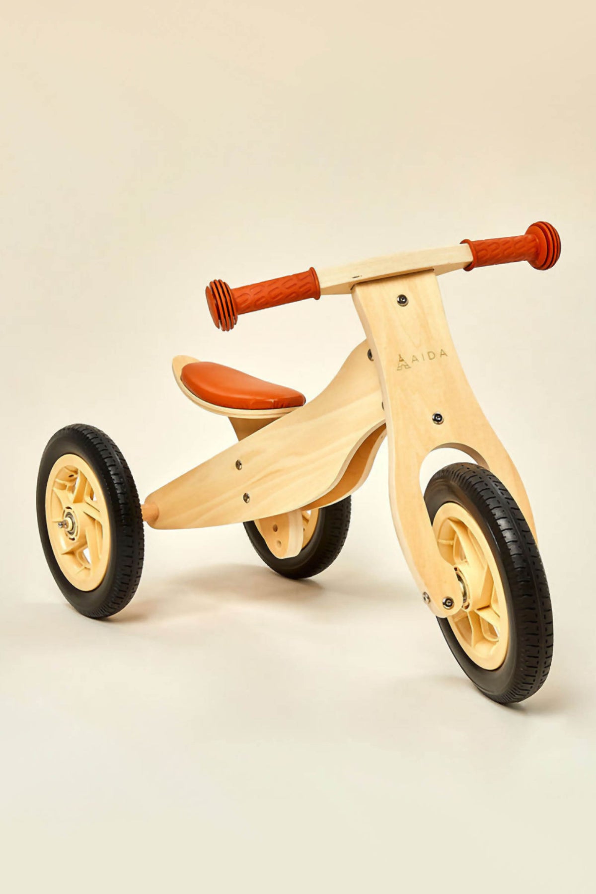 A wooden balance bike with an orange seat and rubber tires, designed for children aged 2 to 4.