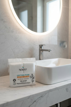 NOLEO Organic Cotton Pads in a resealable bag on a marble bathroom counter next to a white sink.