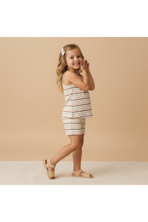 A smiling young girl poses in a striped organic cotton tank top and shorts set, featuring soft neutral colors. The outfit is perfect for playful, sunny days and provides comfort.