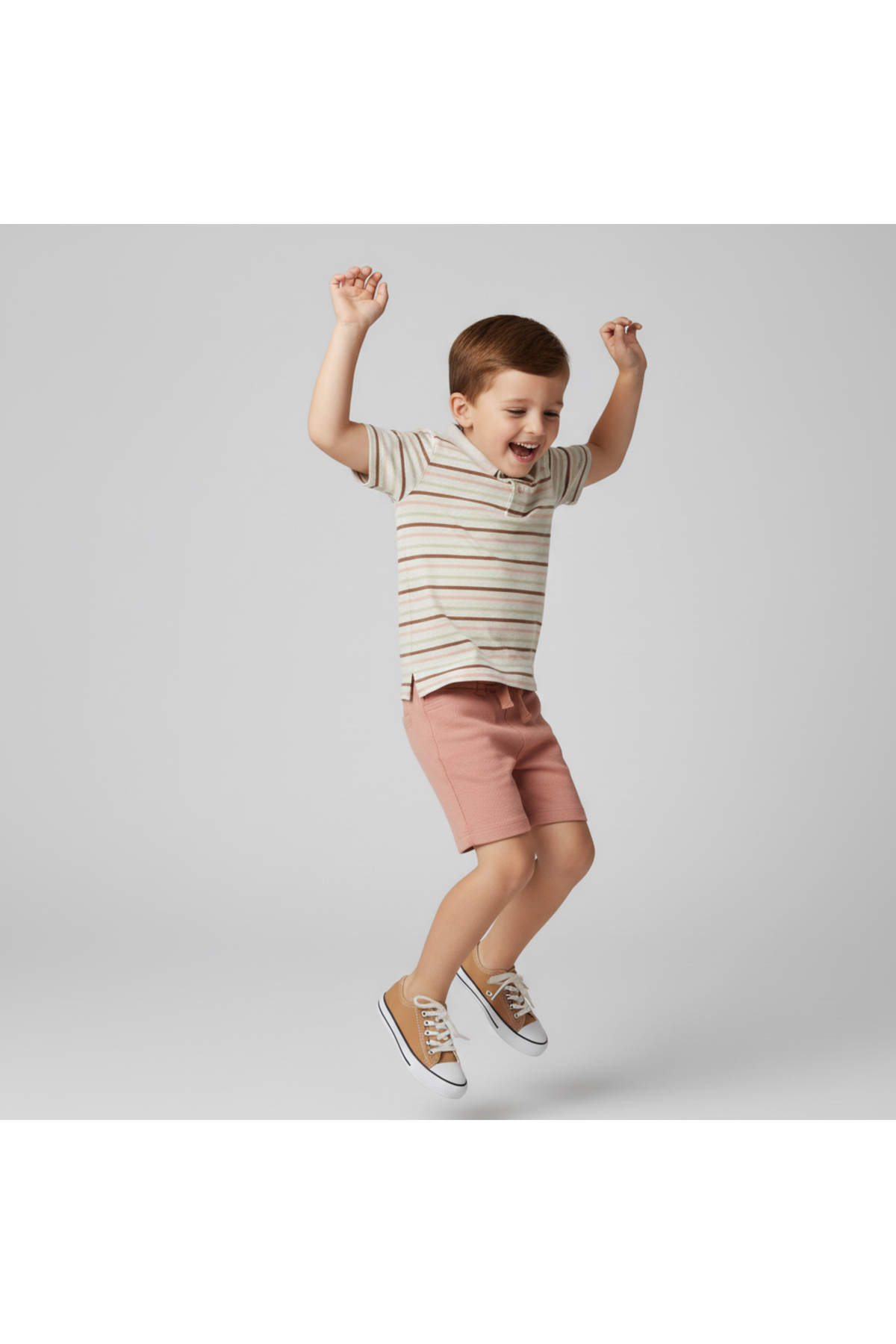 A young boy joyfully jumps while wearing a striped collar tee in soft earth tones and pink shorts. The outfit is crafted from organic cotton, perfect for comfortable play.