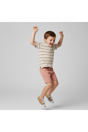 A young boy joyfully jumps while wearing a striped collar tee in soft earth tones and pink shorts. The outfit is crafted from organic cotton, perfect for comfortable play.