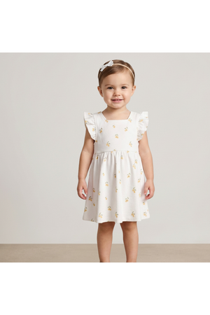 A young girl smiles while wearing a soft, white dress adorned with a cheerful lemon print. The dress features ruffled sleeves, perfect for warm weather and playful activities.