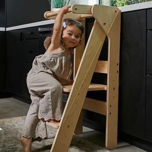 A young child climbs an artificial wood educational tower in a modern kitchen, showcasing its sturdy design and inviting participation in cooking activities.