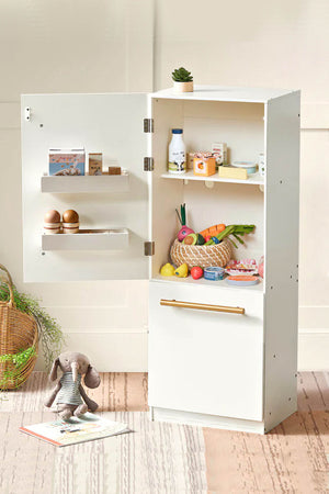 A white wooden play refrigerator stands open, showcasing colorful pretend food items like fruits, vegetables, and eggs on its shelves.