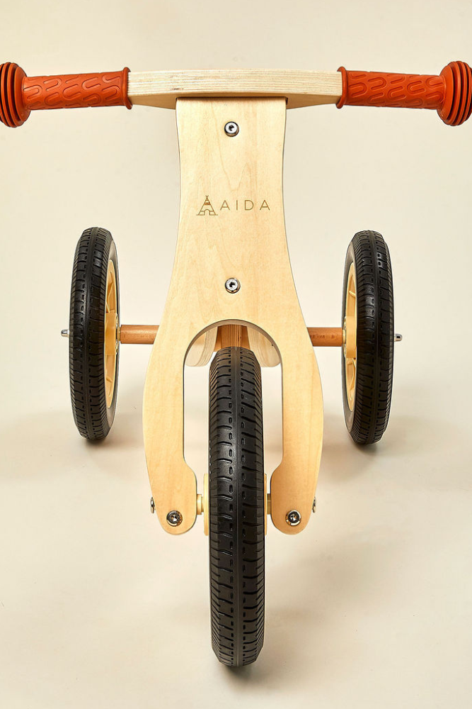 AIDAs 2-in-1 Mini Wooden Balance Bike features a sturdy wooden frame, orange rubber grips, and two wheels, designed for toddlers aged 18 months to 3 years, promoting balance and coordination.