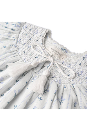 Close-up view of a light blue organic cotton smocked top featuring delicate floral patterns and a textured collar. The top includes playful tassels and is part of the Makemake brand.