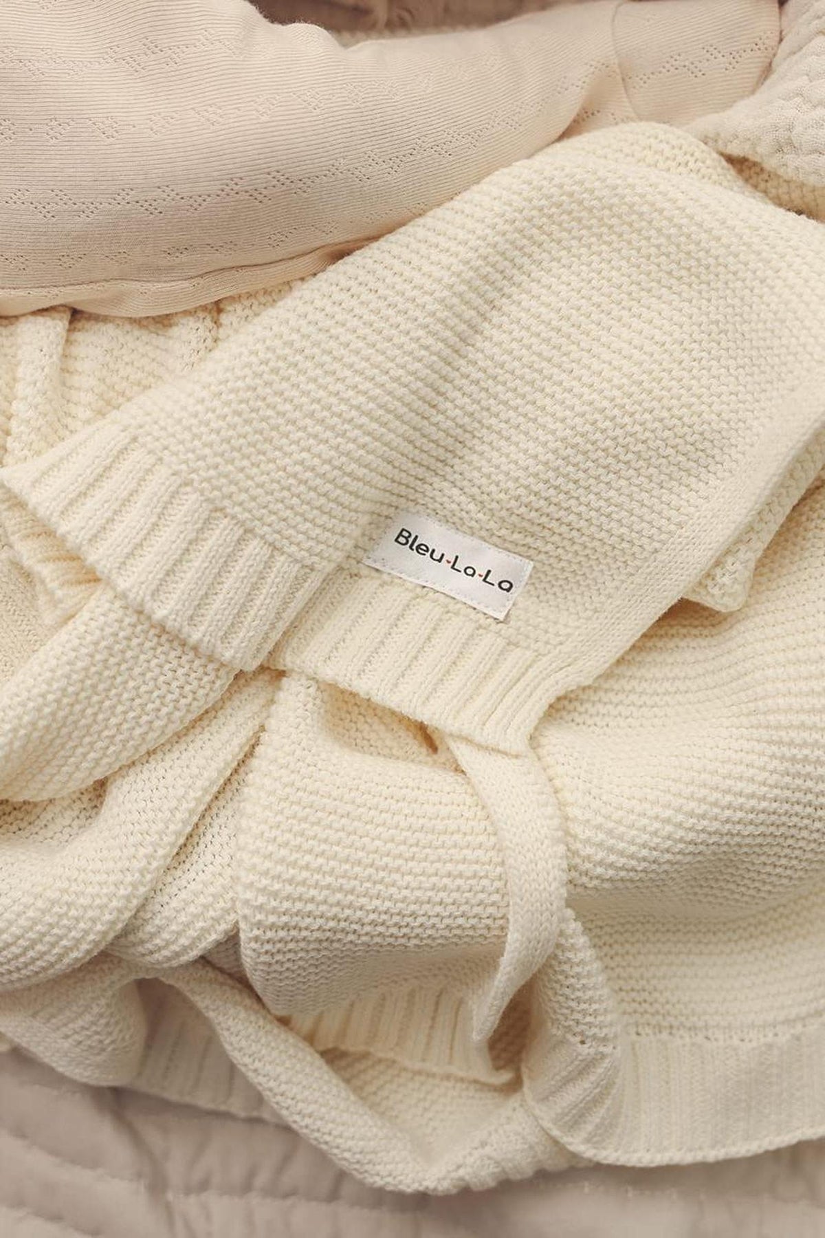 Cream-colored knitted blanket with a Bleu-La-La label, showcasing a soft, textured weave and ribbed edges.