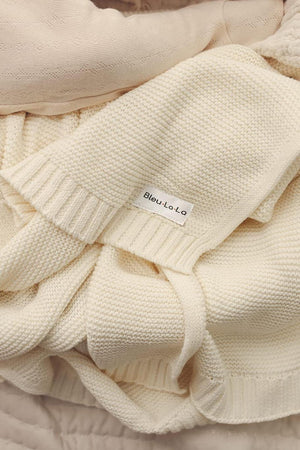 Cream-colored knitted blanket with a Bleu-La-La label, showcasing a soft, textured weave and ribbed edges.