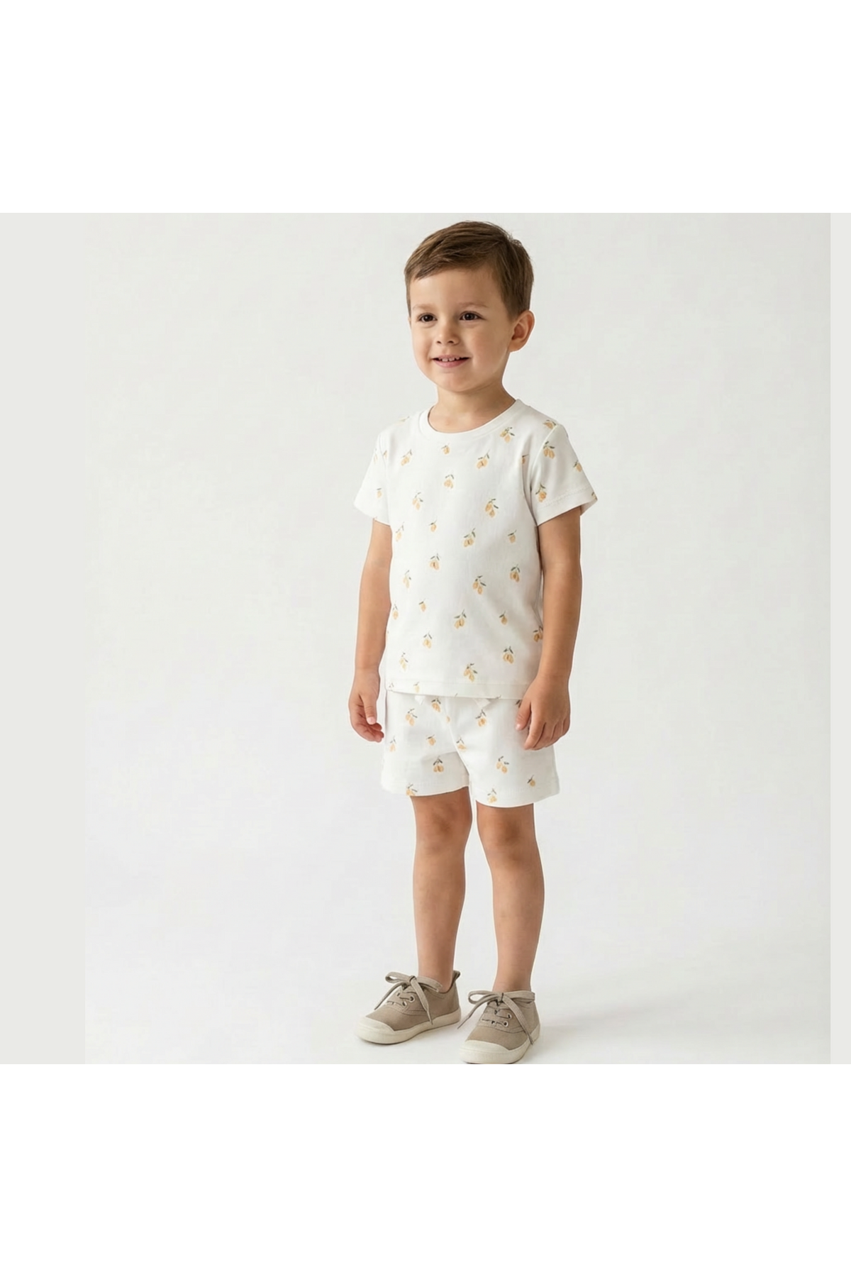 A young boy stands wearing a playful organic cotton tee and shorts set featuring a lemon print.