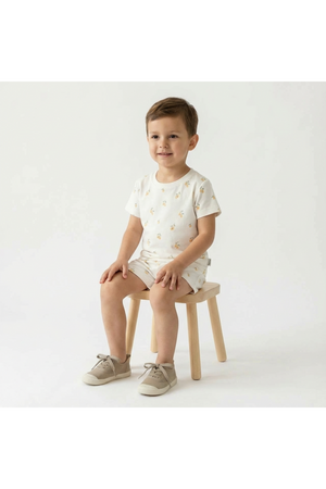 A young child sits on a small wooden chair, wearing a soft, organic cotton tee and shorts set featuring a playful lemon print.