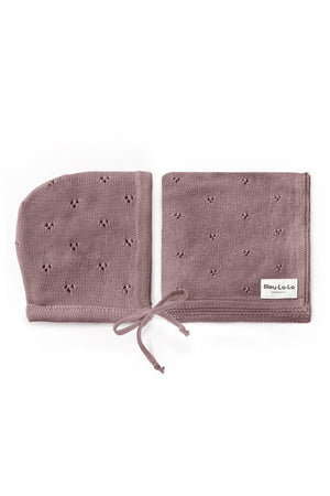 A mauve pointelle swaddle blanket and hat set made from organic cotton, featuring delicate patterns and a tie detail.