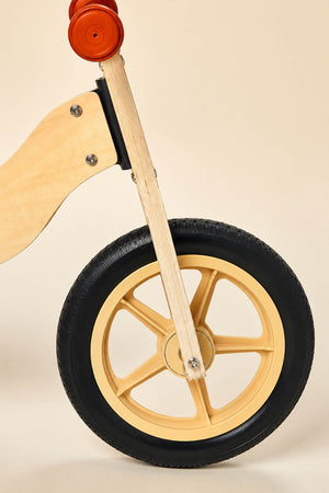 Close-up of the front wheel of a wooden balance bike, featuring a natural wood frame and a durable black tire with a gold rim.