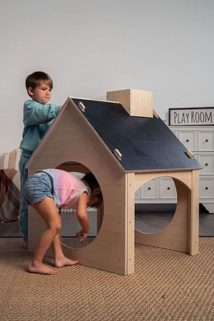 A boy and girl play with an evergreen wooden childrens playhouse featuring a chalkboard roof in a cozy playroom. The house is made from sustainable materials, promoting imaginative play.