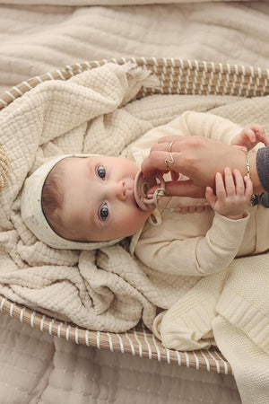 A baby lies in a woven basket with a pacifier, wrapped in a soft, cream-colored knit blanket.