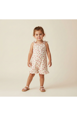 A young girl models a sleeveless, floral ruffle jumpsuit with a light pink background. The outfit features ruffled edges and adjustable shoulder ties, perfect for warm-weather play.
