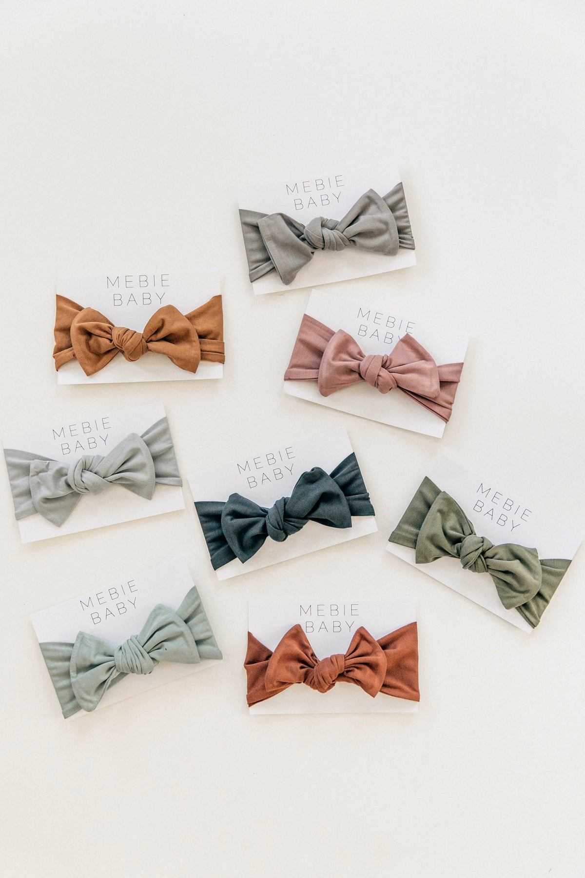 Various Mebie Baby head wraps in earthy tones displayed on cards against a light background.