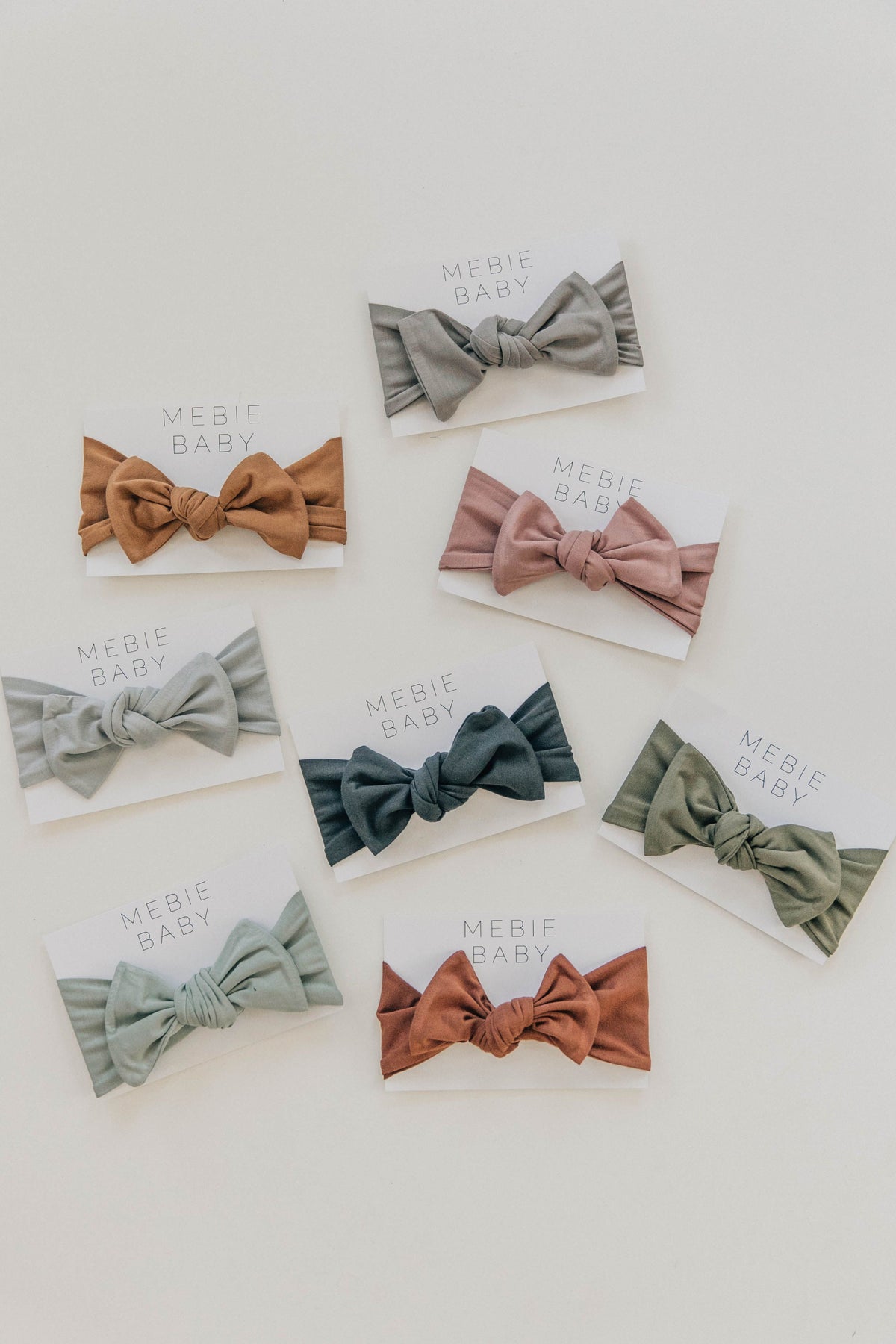 Various colored Mebie Baby head wraps, including sage and rust, displayed on white cards against a plain background.